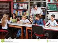 mature teacher teacher showing book schoolboy library happy mature male students studying table student using computer desk classroom